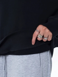 Close-up of silver ring set styled with a black sweatshirt and casual grey trousers