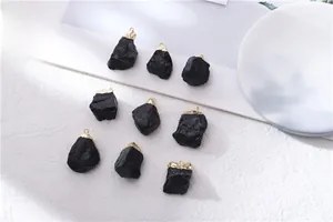 Macro shot of natural raw black tourmaline pendants with gold plated caps on white fabric