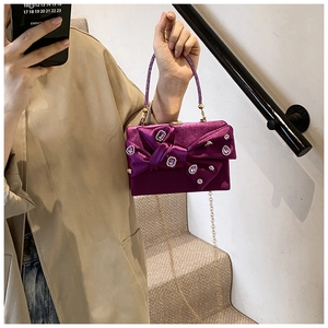 Detail of purple velvet evening clutch featuring a crystal bow and beaded ring handle