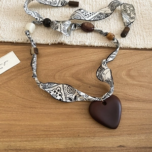 Ethnic bohemian necklace detail with black floral ribbon and dark brown wooden heart pendant