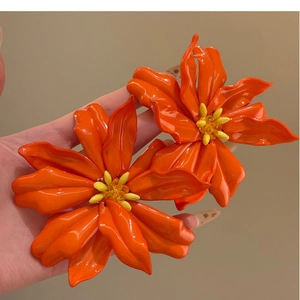 Close-up of vibrant orange acrylic flower earrings with yellow centers and silver pins
