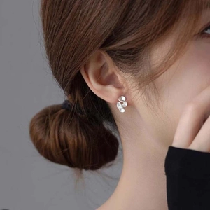 Macro shot of silver petal-shaped earrings with metallic luster on model ear