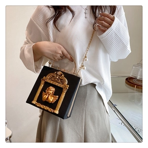 Detail of black box handbag with golden baroque angel relief and pearl chain strap
