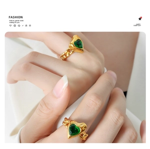 Detail of gold-plated chain rings with heart-shaped green zircon stones on finger