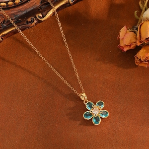Gros plan détaillé du pendentif fleur dorée avec gemmes bleues sur chaîne fine dorée