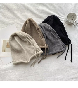 Flat lay of four knit balaclava hats with ear flaps and drawstrings in neutral colors