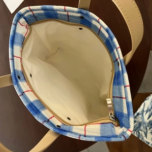 Close-up of blue plaid cotton tote bag showing metal zipper and beige leather handle