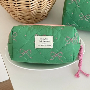 Close-up of green quilted makeup bag with pink bow patterns and a woven logo patch