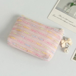 Detailed view of pink tweed coin purse with bow accent and pearl charm on a styled desk