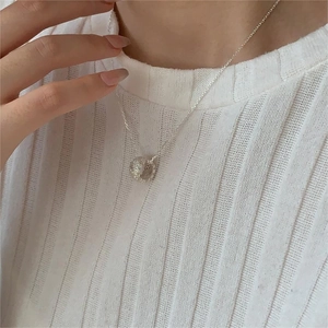 Close-up of a minimalist silver textured bead pendant necklace on a knit sweater
