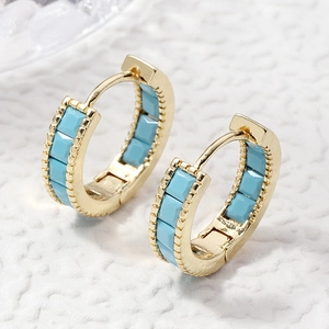 Golden earrings with sky blue stones and beaded texture on a white textured background