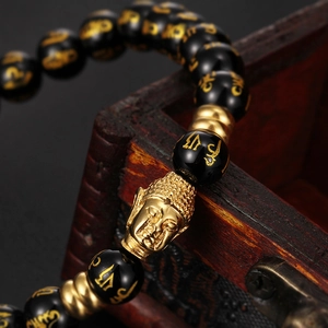 Gros plan d'un bracelet en onyx noir avec tête de Bouddha dorée sur boîte en bois