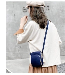 Back view of a model wearing a deep blue nylon crossbody phone bag with gold zippers