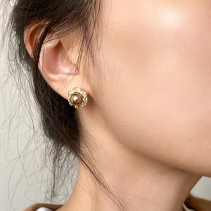 Close-up of vintage golden pearl stud earrings with zircon halo on model's ear
