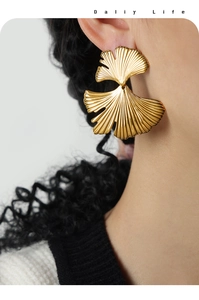 Detail of elegant gold ginkgo leaf earrings with textured metallic finish on a model