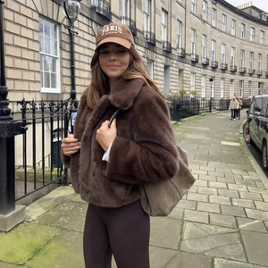 Brown faux fur jacket with matching baseball cap shown in a stylish outdoor street view