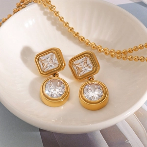 Elegant gold earrings with square and round white zircons displayed on a ceramic plate