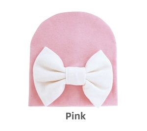 Close-up of pink knit baby beanie with large white bow detail on plain white background