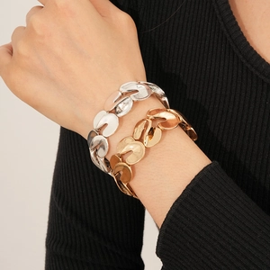 Close-up of gold and silver S-shaped chunky chain bracelets on a model wrist