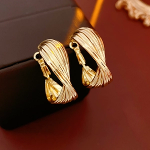 Close-up of golden twisted hoop earrings with a polished metallic finish on a dark background