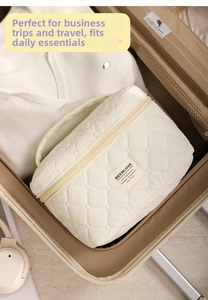 Detailed top view of a cream quilted cosmetic bag with handle inside a travel suitcase