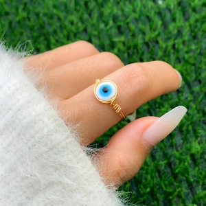 Macro shot of handmade gold wire-wrapped evil eye ring on hand with blue stone