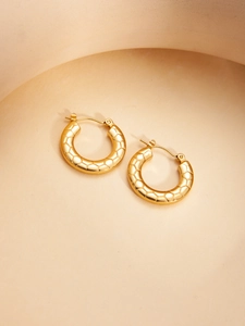 Detail of gold hoop earrings with honeycomb texture on a warm beige background