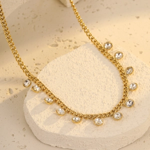 Close-up of gold cuban chain necklace with eleven round clear crystal charms on white stone