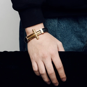 Detail of a men's braided leather bracelet featuring a textured golden stainless steel cross