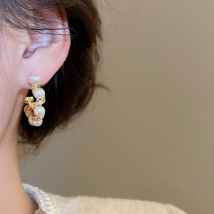 Detail of gold spiral earrings featuring white pearls and crystals worn by a model