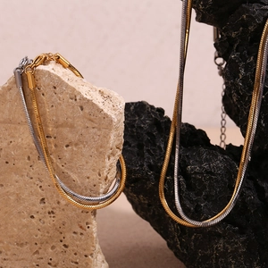 Detailed view of dual-tone snake chain necklaces in gold and silver over textured rocks