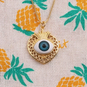 Collier doré avec pendentif cœur et détail œil bleu sur fond en tissu beige