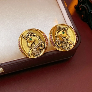 Macro view of vintage gold unicorn earrings with green and pink gemstones on brown leather