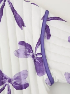 Detailed close-up of quilted cotton fabric with purple floral bow print and piping edges