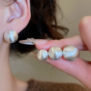 Close-up of brushed silver round stud earrings showing three sizes and cat-eye texture