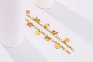 Dettaglio di bracciale a sfere dorate con ciondolo moneta su blocchi geometrici bianchi
