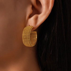 Detail of gold-tone mesh texture C-shaped hoop earrings on a female model