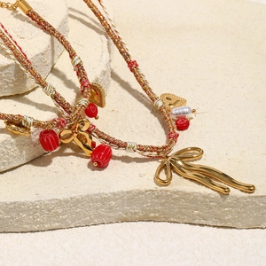 Macro shot of 18K gold plated butterfly pendant on red and beige woven cotton cords