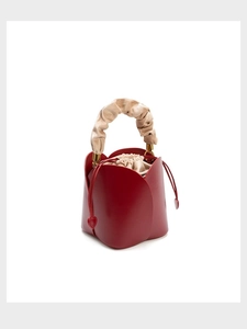 Detail of red petal-shaped bucket bag featuring a beige ruffled handle and heart charm