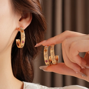 Detailed shot of gold-plated C-shape earrings with colorful gemstone flowers on a model