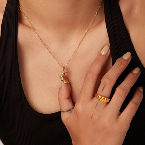 Close-up of a crescent moon pendant necklace and textured ring on a model