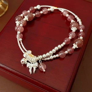 Dettaglio del bracciale con perle di quarzo fragola e ciondolo a fiocco su scatola regalo