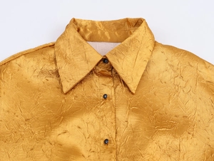 Detail van de gouden satijnen stof met geplooid ontwerp en zwarte knoop op de kraag