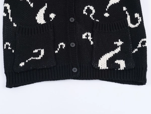 Detail of black knit cardigan featuring white question mark patterns and round buttons