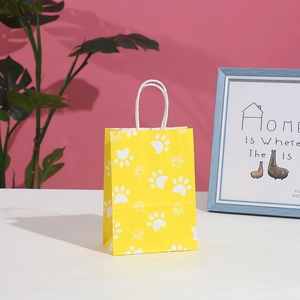 Yellow kraft paper gift bag with white paw prints and woven handles for birthday parties