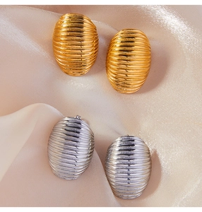 Close-up of gold and silver textured oval stud earrings on soft satin fabric