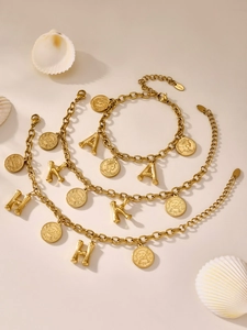 Detailed macro of gold stainless steel link bracelets with initial charms and coin pendants