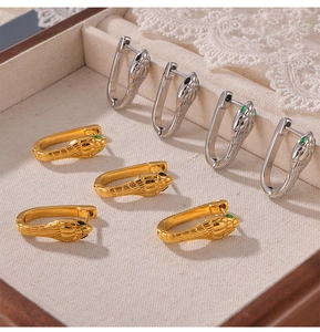 Macro detail of snake-head U-shaped earrings in gold and silver with green gem eyes