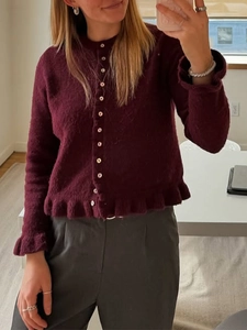 Detail of burgundy knit cardigan featuring button closure and ruffled hem and cuffs