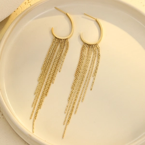 Close-up of golden geometric tassel earrings with long metal chains on a beige tray